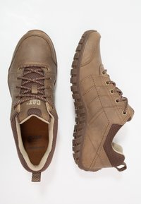 Braune Schnürschuhe mit strukturiertem Finish, ausgestattet mit einem gepolsterten Kragen, braunen Schnürsenkeln und einer robusten Gummisohle für optimale Rutschfestigkeit.
