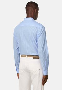 Chemise rayée bleue clair avec un col boutonné, des manches longues et un dos uni. Portée avec un pantalon blanc et une ceinture tressée.