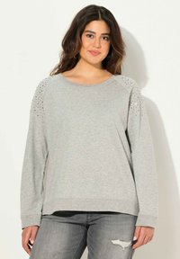 Felpa grigia con maniche lunghe, scollo rotondo e dettagli con borchie sulle spalle. Abbinata a jeans grigi leggermente sdruciti.