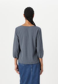 Marinebluse mit dreiviertel Puffärmeln, Rundhalsausschnitt und strukturiertem Stoff. Kombiniert mit einem Denimrock.