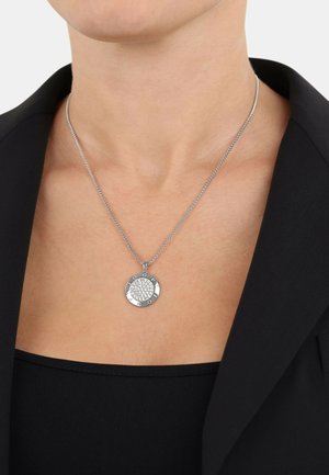 Collar de plata con un colgante redondo que presenta múltiples piedras claras, unido a una cadena delgada, llevado sobre una blusa negra.