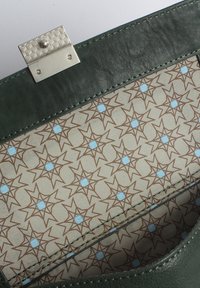 Grüne Leder-Clutch mit einem silbernen metallischen Verschluss. Das Innere zeigt ein sich wiederholendes braunes und hellblaues Sternmuster auf einem cremefarbenen Stoff.
