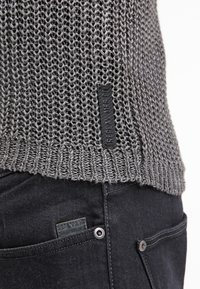 Maglione grigio a maglia con una trama strutturata e orlo a costine. Include un dettaglio con etichetta nera. Abbinato a pantaloni in denim scuro con un'etichetta logo.