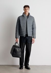 Pelēks pūkains mētis ar augstu apkakli, kombinēts ar pelēku augšu un tumšām biksēm. Modelis tur melnu ādas rokassomu.