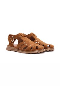 Sandalias de ante marrón con diseño recortado, acentos de tachuelas metálicas, hebilla ajustable y suelas de goma para tracción. Estilo casual.