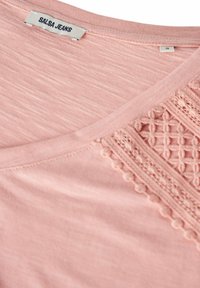 Camiseta rosa con diseño de cuello en V, que presenta un detalle de encaje texturizado en un lado y una tela suave, ligeramente jaspeada.