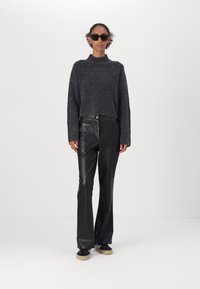 Maglione grigio corto a maglia con maniche lunghe abbinato a pantaloni in pelle neri a vita alta. La modella indossa occhiali da sole neri e scarpe con platform.