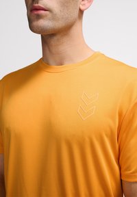 Orange idrottströja med texturerad tyg, korta ärmar och en subtil präglad triangel-logotyp på vänster bröst.