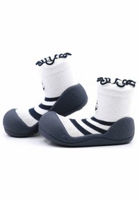 Zapatos de suela de goma gris con un calcetín a rayas blancas y azul marino, que presenta un diseño de puño con volantes. La suela tiene detalles texturizados para mayor agarre.