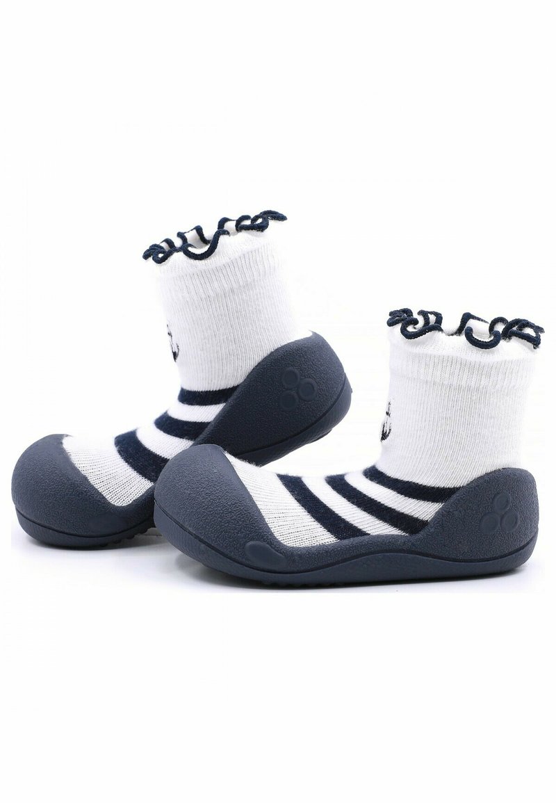 Zapatos de suela de goma gris con un calcetín a rayas blancas y azul marino, que presenta un diseño de puño con volantes. La suela tiene detalles texturizados para mayor agarre.