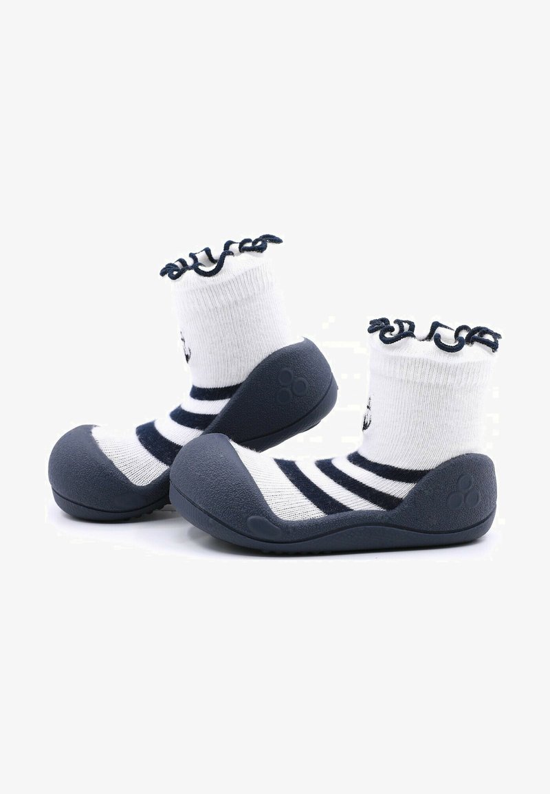 Zapatos de suela de goma gris con un calcetín a rayas blancas y azul marino, que presenta un diseño de puño con volantes. La suela tiene detalles texturizados para mayor agarre.