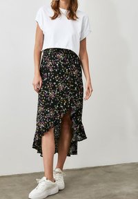 Zwarte bloemenrok met een gerimpelde zoom, voorzien van kleurrijke bloemenpatronen. Gecombineerd met een cropped wit t-shirt en witte sneakers.