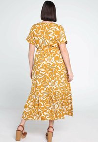 Żółta maksi sukienka w kwiaty z krótkimi rękawami, zebranym w pasie i falbaniastym dołem. Wzór przedstawia białe abstrakcyjne kwiaty na jednolitym tle.