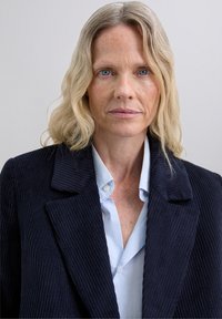 Navy corduroy blazer with wide lapels, paired with a light blue button-up shirt. Smooth texture and vertical ribbing detail visible.