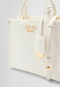 Sac à main matelassé blanc avec quincaillerie dorée. Équipé de doubles poignées, d'une bandoulière amovible et d'un logo de marque. Texture lisse avec un minimum de détails.