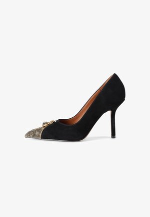 Escarpin à talon haut en daim noir avec un bout pointu orné de clous dorés et une boucle décorative dorée à l'avant.