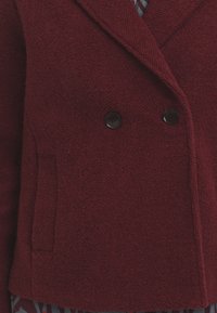 Bordó dvouřadý blazer vyrobený z texturované tkaniny, s dvěma černými knoflíky a boční kapsou.
