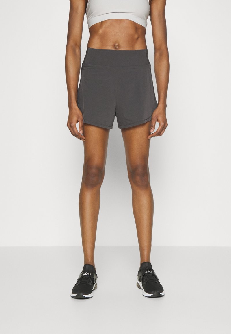 Bermudas deportivas grises con una textura suave y una cintura elástica, combinadas con zapatillas negras. Diseño minimalista, adecuado para deportes o ejercicio.