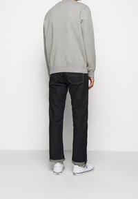 Szary sweatshirt z okrągłym dekoltem w zestawieniu z ciemnymi dżinsami z podwiniętymi mankietami. Białe sneakersy dopełniają stylizację.