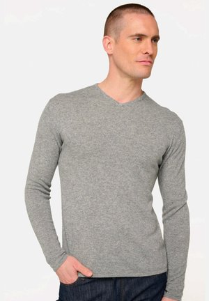 Pull en V gris à manches longues en tissu tricoté doux, avec une coupe ajustée et une texture subtile. Porté avec un jean foncé.