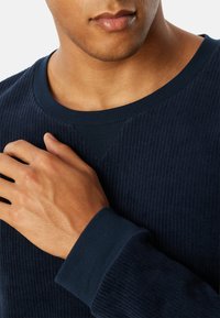 Mørkeblå ribbet sweatshirt med rund hals, der har struktureret stof og en trekantet detalje på skulderen.