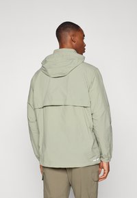 Light green hooded jacket with a back vent, elastic cuffs, and reflective accents near the hem. Made of lightweight, textured fabric.