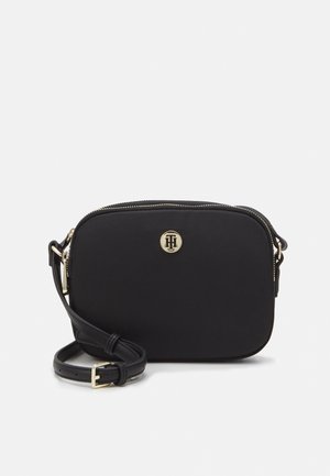 Sort rektangulær crossbody-taske med lynlås i guldton, justerbar rem og lille rundt guldlogoemblem i midten foran.