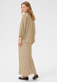 L'ensemble deux pièces beige se compose d'un haut ample à manches trois-quarts et d'une longue jupe avec une fente sur le côté, complété par des ballerines noires.