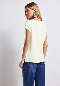 Camiseta de manga corta de color crema claro con un ajuste relajado, combinada con jeans de pierna ancha de tono azul medio. Textura suave y diseño minimalista.