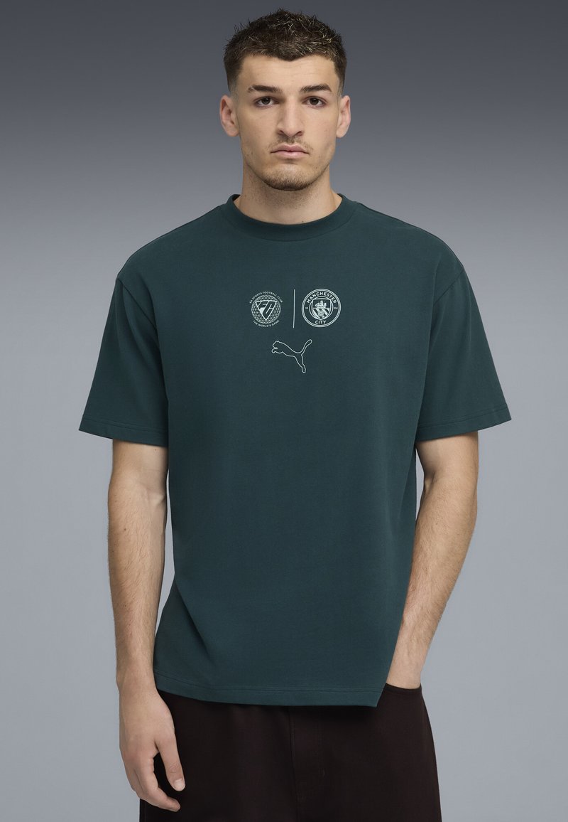 Camiseta de algodón verde con mangas cortas, con cuello redondo y logotipos impresos en blanco en el pecho, incluido el logotipo de Puma.
