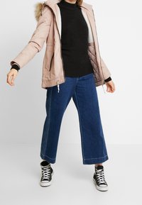 Jasnoróżowa kurtka parka z futrzanym kapturem, połączona z czarnym swetrem i niebieskimi szerokimi dżinsami. Czarnobiałe wysokie trampki dopełniają stylizację.