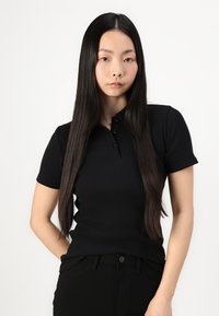 Svart räfflad polo med korta ärmar och knäppning med tre knappar, tillsammans med svarta texturerade byxor. Slät tyg och figurnära design.