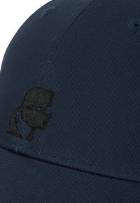 Marinblå keps i texturerat tyg med en svart broderad profildesign. Kepsen har synliga sömmar och en böjd skärm.