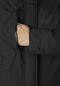 Veste noire avec une poche zippée sur la poitrine, tissu texturé et ajustement sécurisé au niveau des poignets.