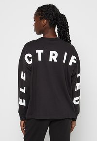 Czarna bluza z długim rękawem z dużym napisem "ELECTRIFIED" w białych literach na plecach i rękawie. Wykonana z miękkiego, teksturowanego bawełnianego materiału.