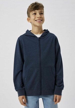 Haut à capuche zippé bleu marine avec une fermeture éclair sur le devant, deux poches latérales et une capuche. Fabriqué à partir d'un tissu lisse et léger.