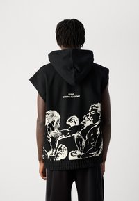 Person wearing black sleeveless hoodie with white boxing-themed graphic and "HUGO BOXING ACADEMY" text on the back.