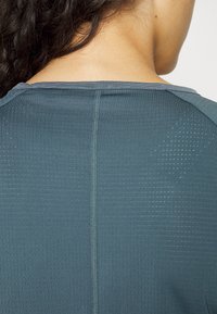 Kortärmad teal färgad träningsskjorta med ett texturerat mönster, med rund hals och en synlig söm som går ner längs ryggen.