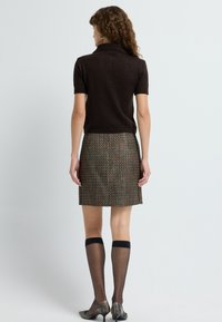 Hnědá polo tričko s krátkým rukávem doplněné vzorovanou hnědou sukní. Černé podkolenky a metalické boty na podpatku dotvářejí celý outfit.