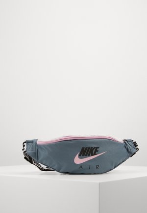 Riñonera Nike Air azul y rosa con logo negro y correa ajustable sobre pedestal blanco contra fondo liso.
