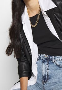 Svart konstläderjacka med en vit skjorta under, parat med en svart ribbad topp och ljusblå högmidjade jeans. Guld kedja halsband.