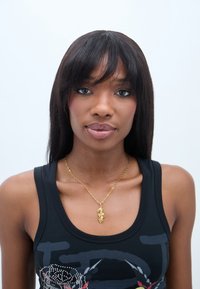 Colier din aur cu un pandantiv răsucit, purtat peste un top fără mâneci de culoare neagră, cu un design grafic. Textură netedă, finisaj metalic strălucitor.