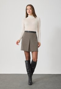 Feszes fehér garbó, barna kockás mini szoknyával párosítva, fekete övvel kiemelve; a modell fekete térd fölötti csizmát visel.