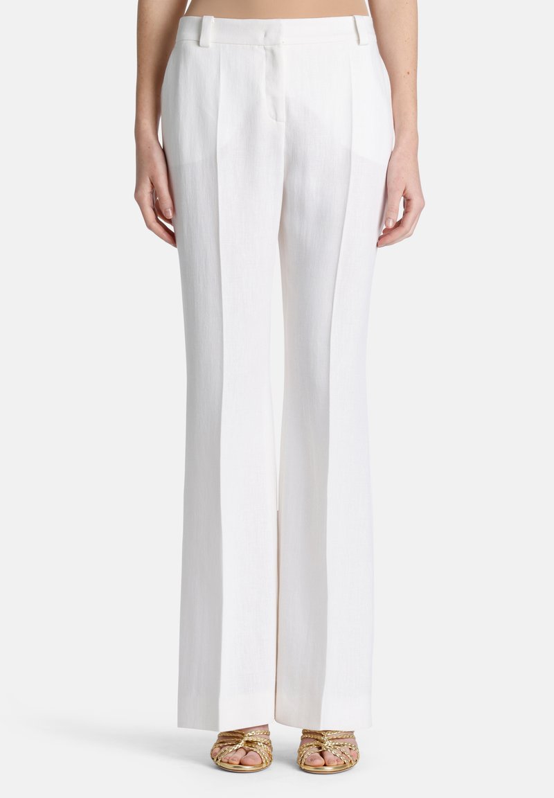 Witte linnen broeken met een hoge taille, voorzien van voorvouwen en een recht model, gecombineerd met gouden sandalen met bandjes.
