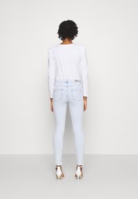 Jeans skinnies de color azul claro con cintura alta y dobladillo deshilachado, combinados con una blusa blanca de manga larga. Presenta un diseño minimalista y cinco bolsillos.