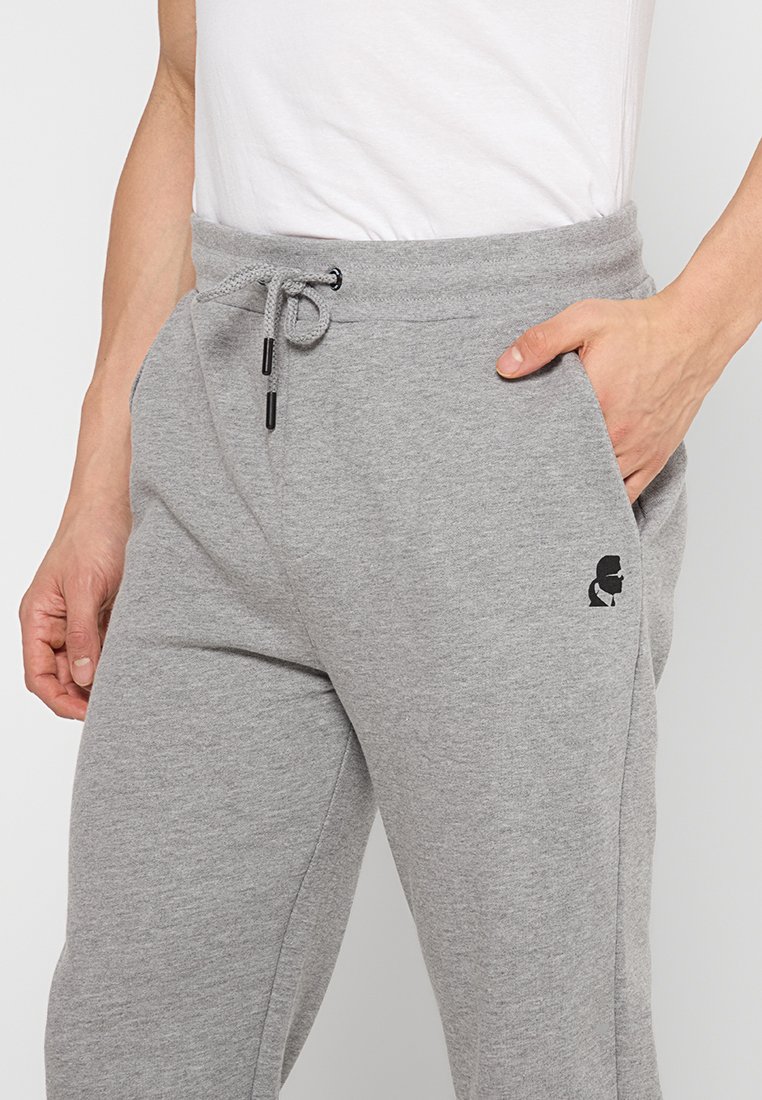 Pantalones de chándal grises, hechos de una suave mezcla de algodón, con una cintura elástica con cordón y un sutil logo negro en el lateral.