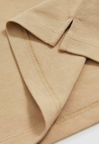Beige bomuldsstof med en blød tekstur, der har foldede ærmer og pæne sømme, hvilket fremhæver en glat overflade og let design.