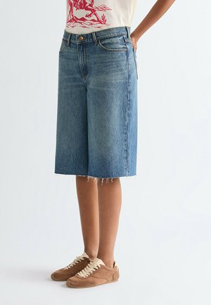 Blå denim culottes med frynset kant, der har en afslappet pasform og fem-lomme-design, båret med brune ruskindssneakers.
