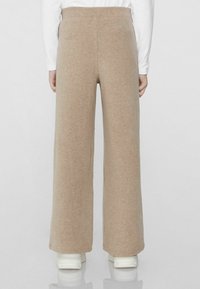 Beige, weit geschnittene Hose aus weichem Stoff mit elastischem Bund, kombiniert mit weißen Schuhen für einen lässigen Look.