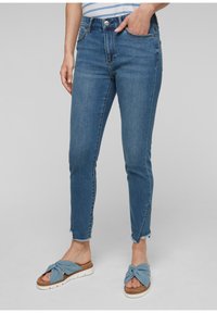 Ljusblå jeans i slim fit med midja av medelhöjd och fransdetaljer. I kombination med blå knutsandaler med vit sula.